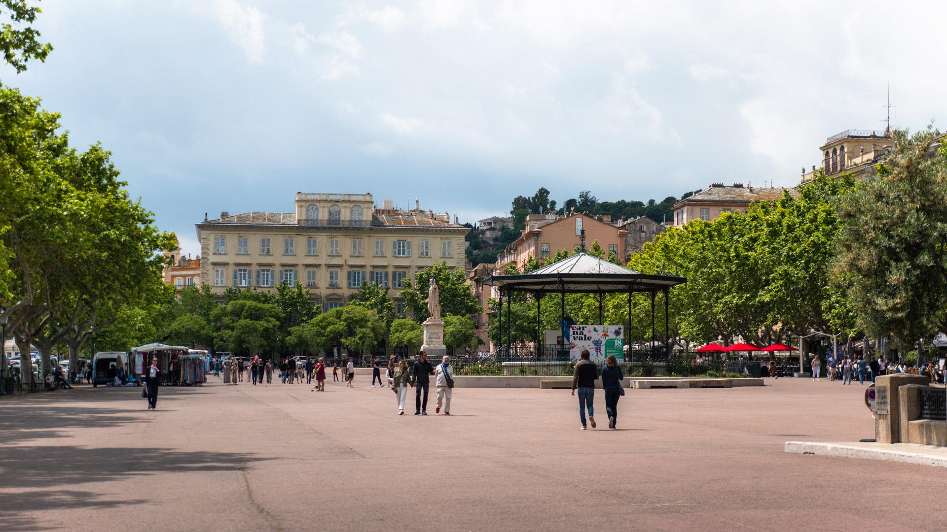 Wide view of Place Saint-Nicolas in Bastia with trees, cafés and people strolling.
