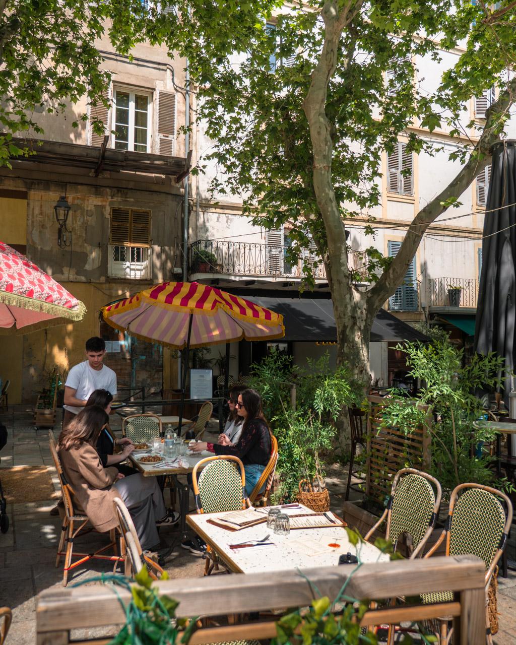 People relaxing at café tables in a sunlit square in Terra Vecchia.