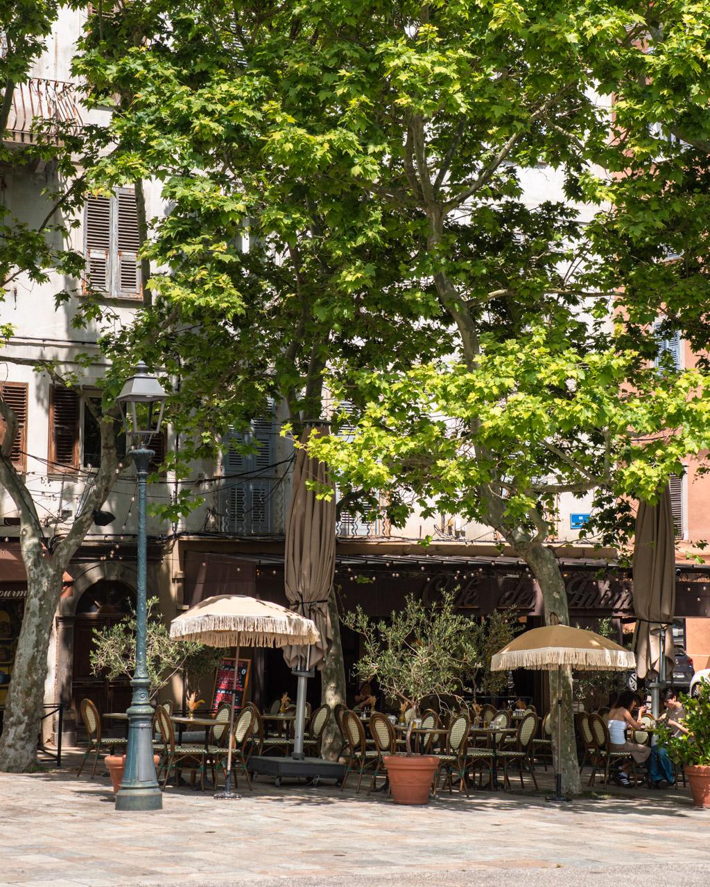 Tree-shaded Place du Marché in Bastia with benches and cafés lining the square.