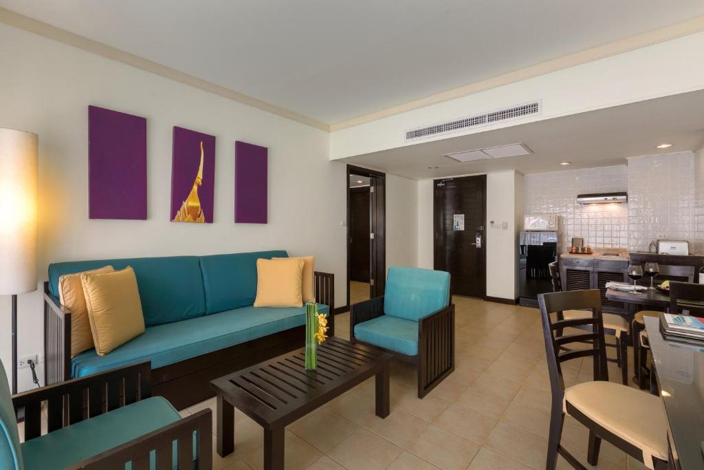 Centara Kata Phuket family suite living room with teal sofa, dark wood furniture, purple artwork, and open kitchen area.