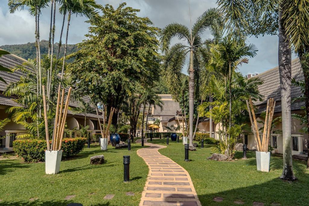 Lush tropical grounds at Centara Kata Phuket resort with brick pathway, palm trees, manicured lawns, and traditional Thai architecture buildings.