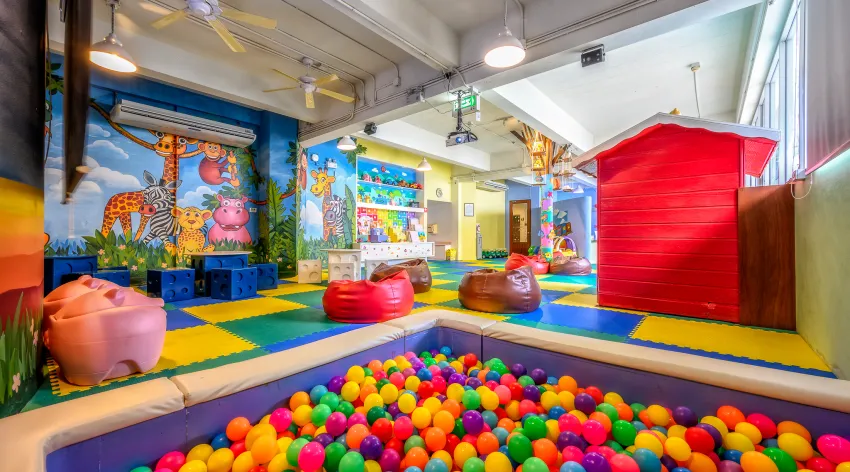 Bright kids' club interior with colorful ball pit, animal murals, bean bags, toy structures, and vibrant floor matting at Centara Kata Phuket resort.