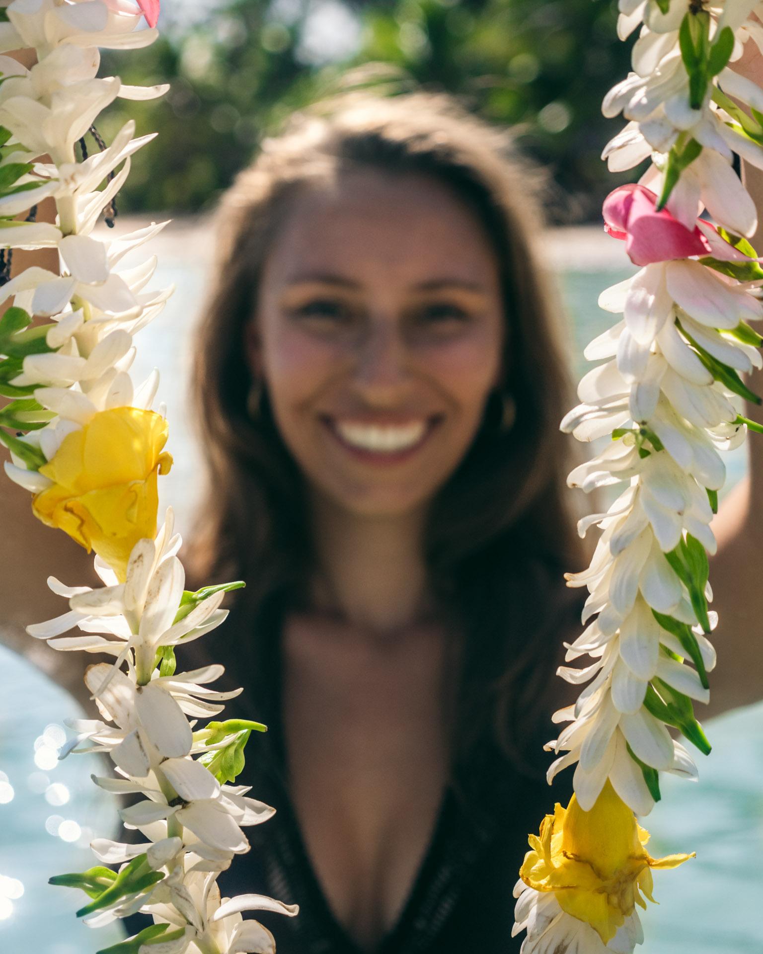 Victoria holding a lei (flower necklace) up to the camera, with a tropical beach blurred behind her.