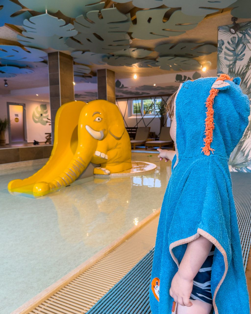 Adrian in a towel poncho pointing at the yellow elephant slide in the pool at Leiners