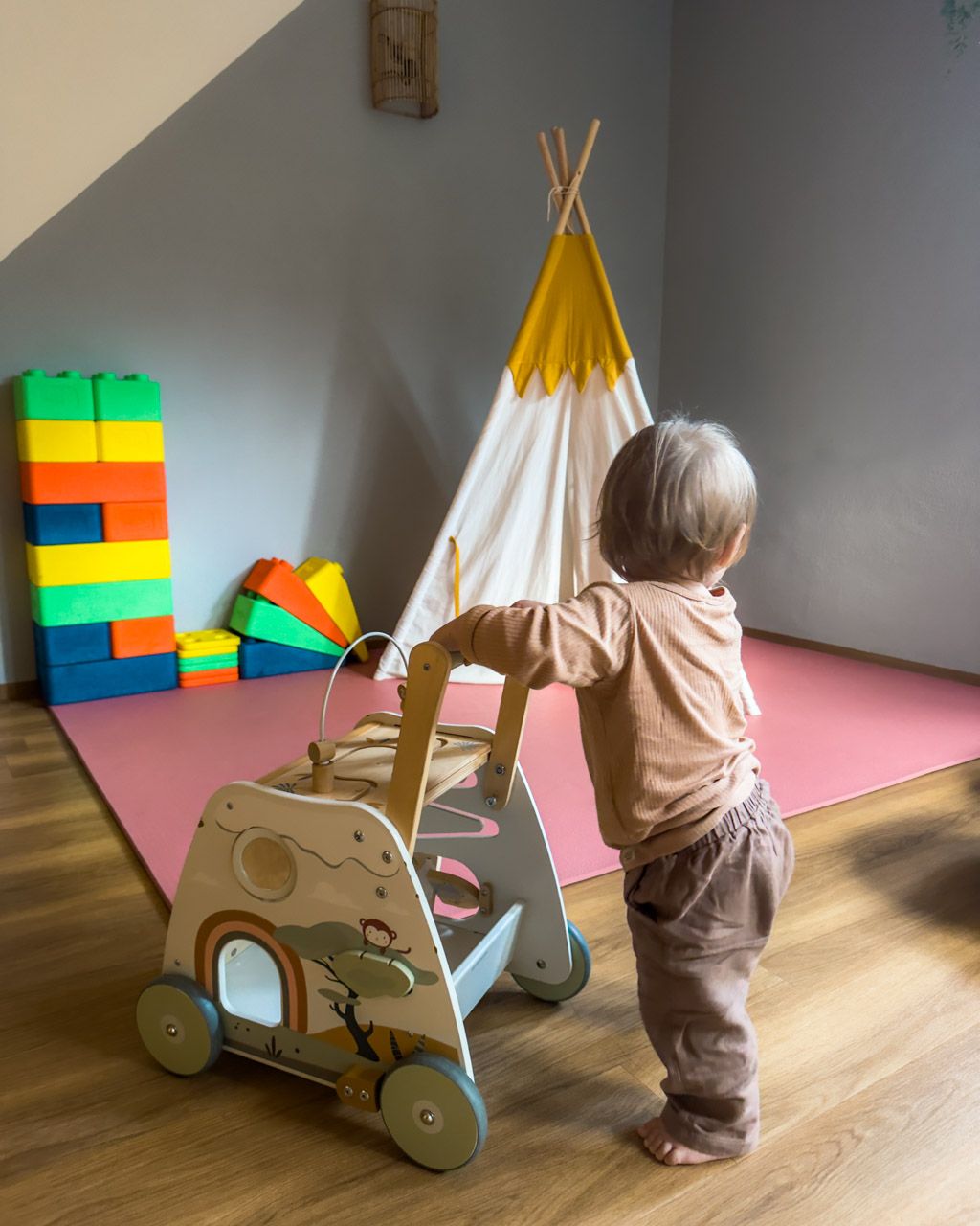 Zoe pushing a wooden walker wagon in the baby playroom at Leiners