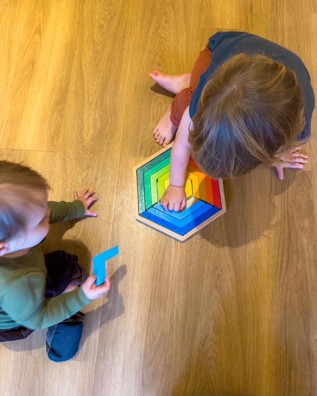 Adrian and Zoe playing with a wooden rainbow puzzle on the playroom floor