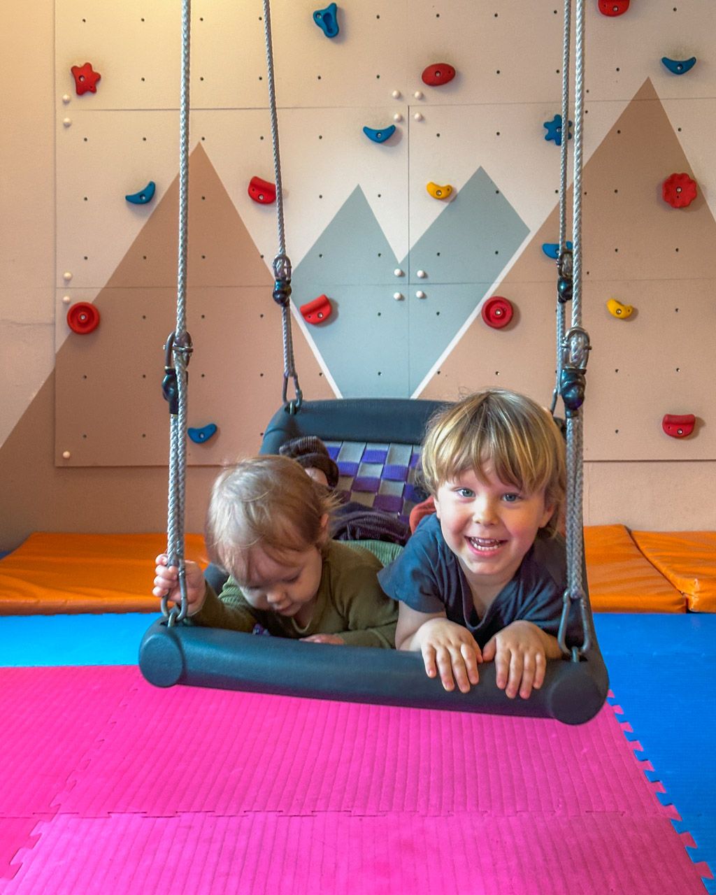 Adrian and Zoe on the swing in the soft-play room, with the climbing wall behind