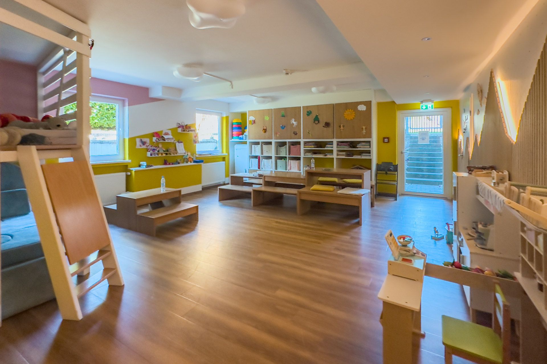The main childcare room at Leiners with low benches, a play kitchen and a reading loft
