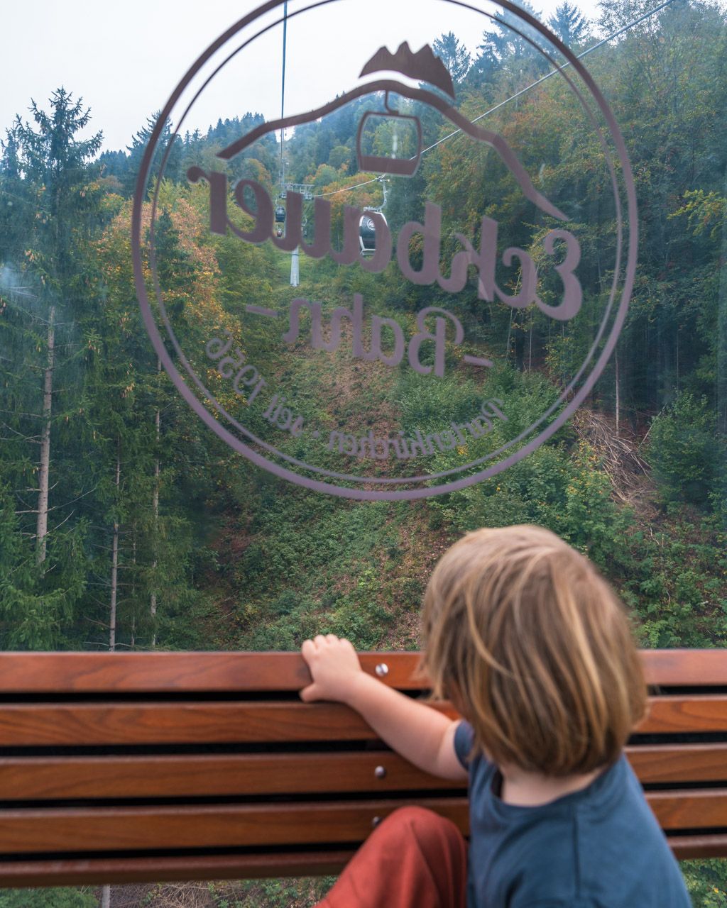 Child looking out of the Eckbauerbahn cabin with the lift logo etched in the glass