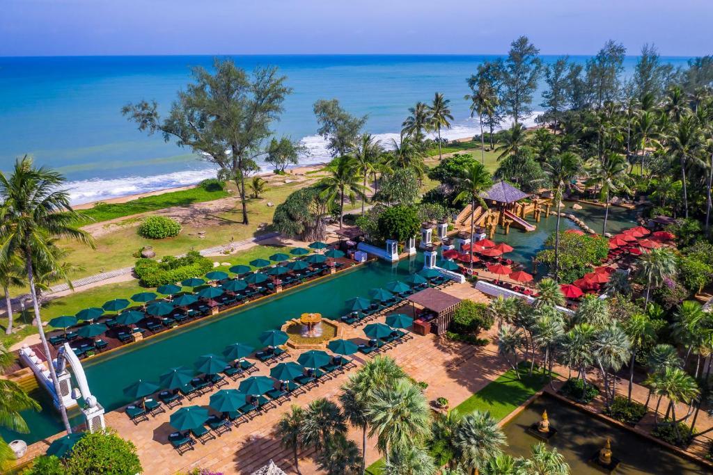 Aerial view of JW Marriott Phuket resort with turquoise pools, red umbrellas, palm trees, and Andaman Sea beach beyond.