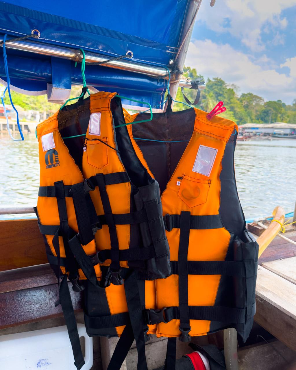 Orange and black life jackets hanging on blue boat canopy at Kuan Tung Ku Pier, tropical waters and mangroves visible.