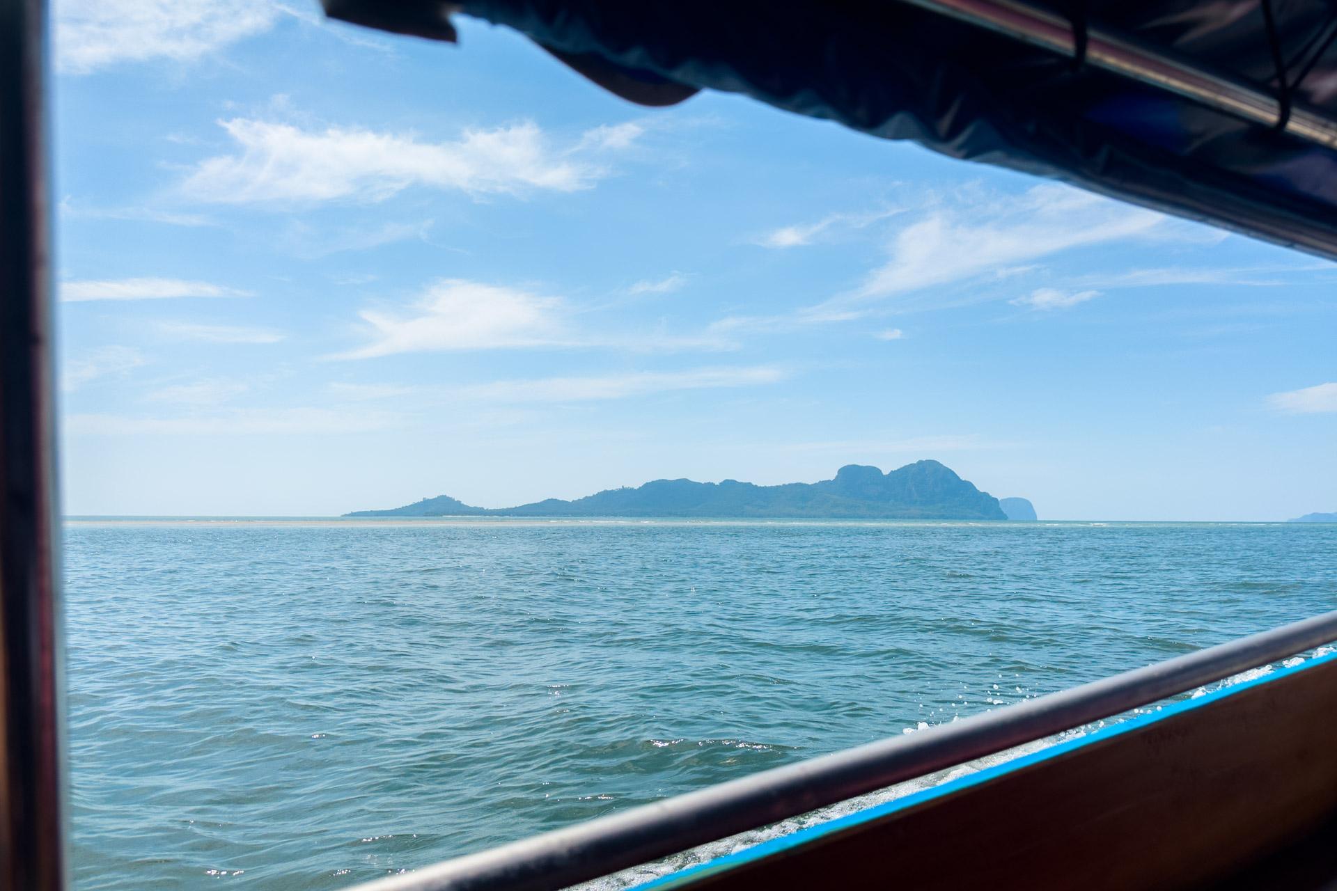 View from boat of Koh Mook island with limestone cliffs across the turquoise waters of the Andaman Sea under clear sky.