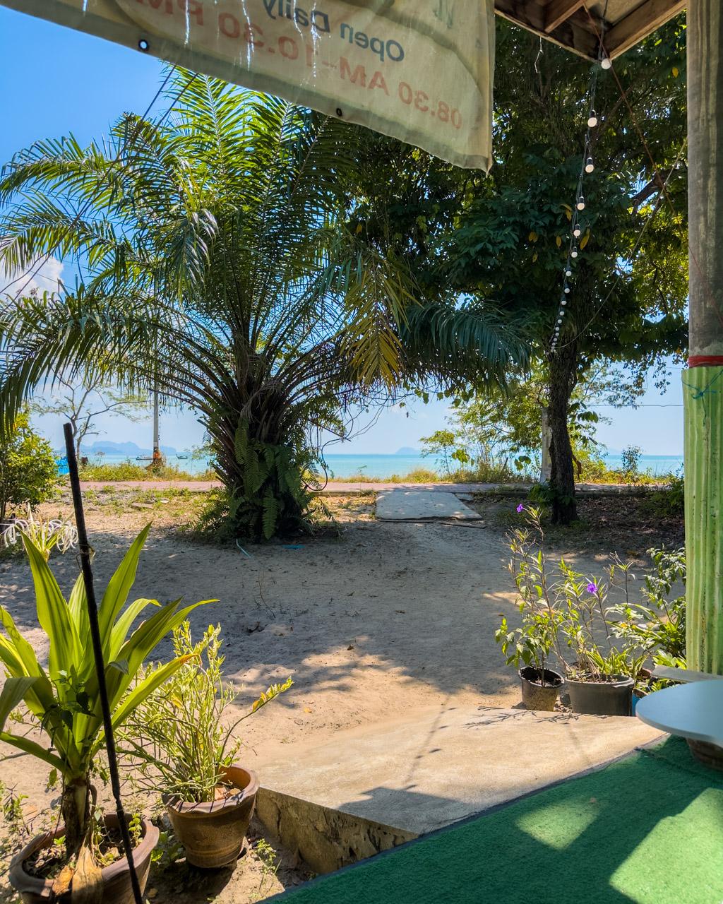 Shaded beachfront patio with palm trees overlooks turquoise waters and distant islands at Koh Mook, Thailand.