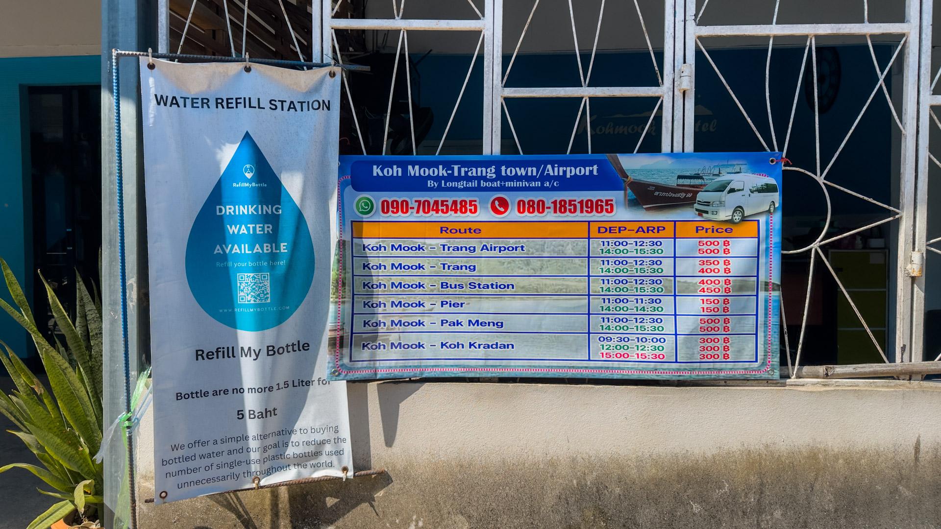 Water refill station and boat transport signs at Koh Mook, Thailand, showing where to refill drinking water and the ferry schedule to Trang Airport.