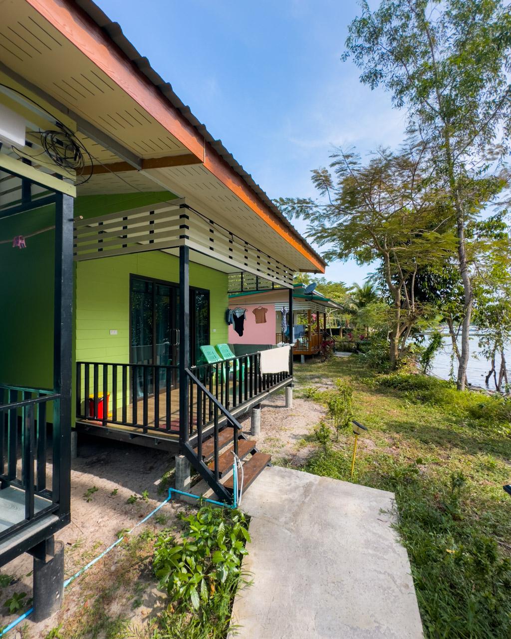Colourful family bungalow exterior at Kohmook Happy Time, with lime-green and pink walls and tropical trees behind.