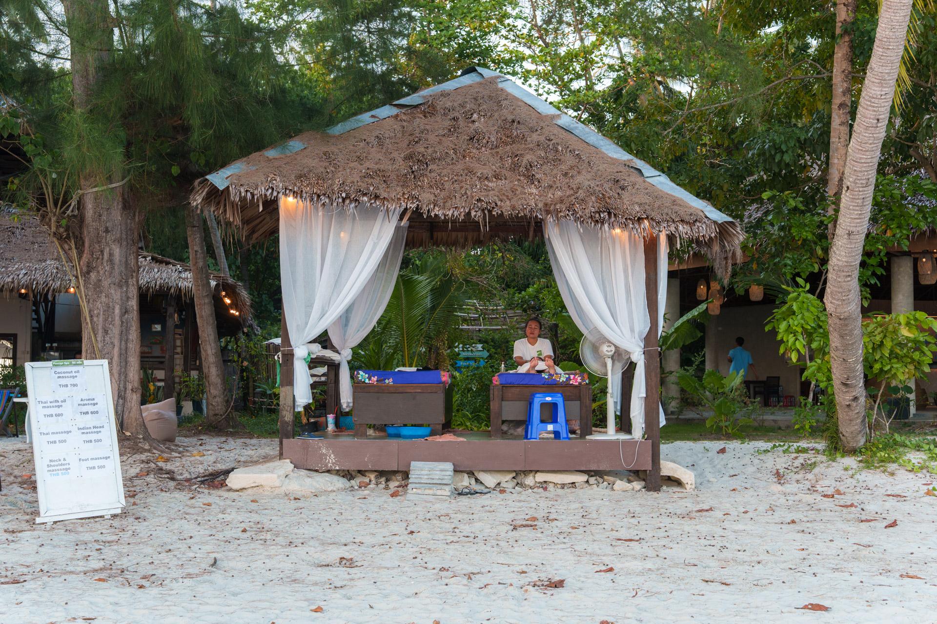 Beachfront massage pavilion with thatched roof and white curtains on Koh Mook island, Thailand.