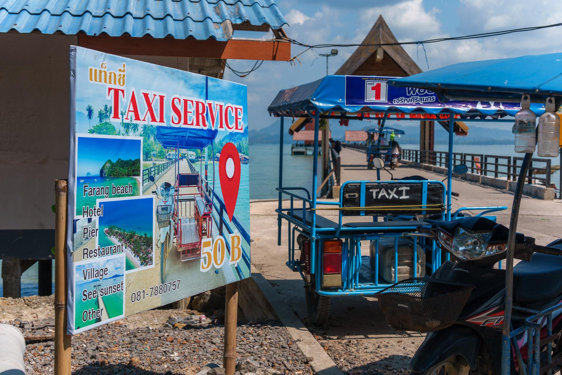 Sign saying a tuk-tuk "taxi" is 50 baht on Koh Mook, next to a tuk-tuk by the pier