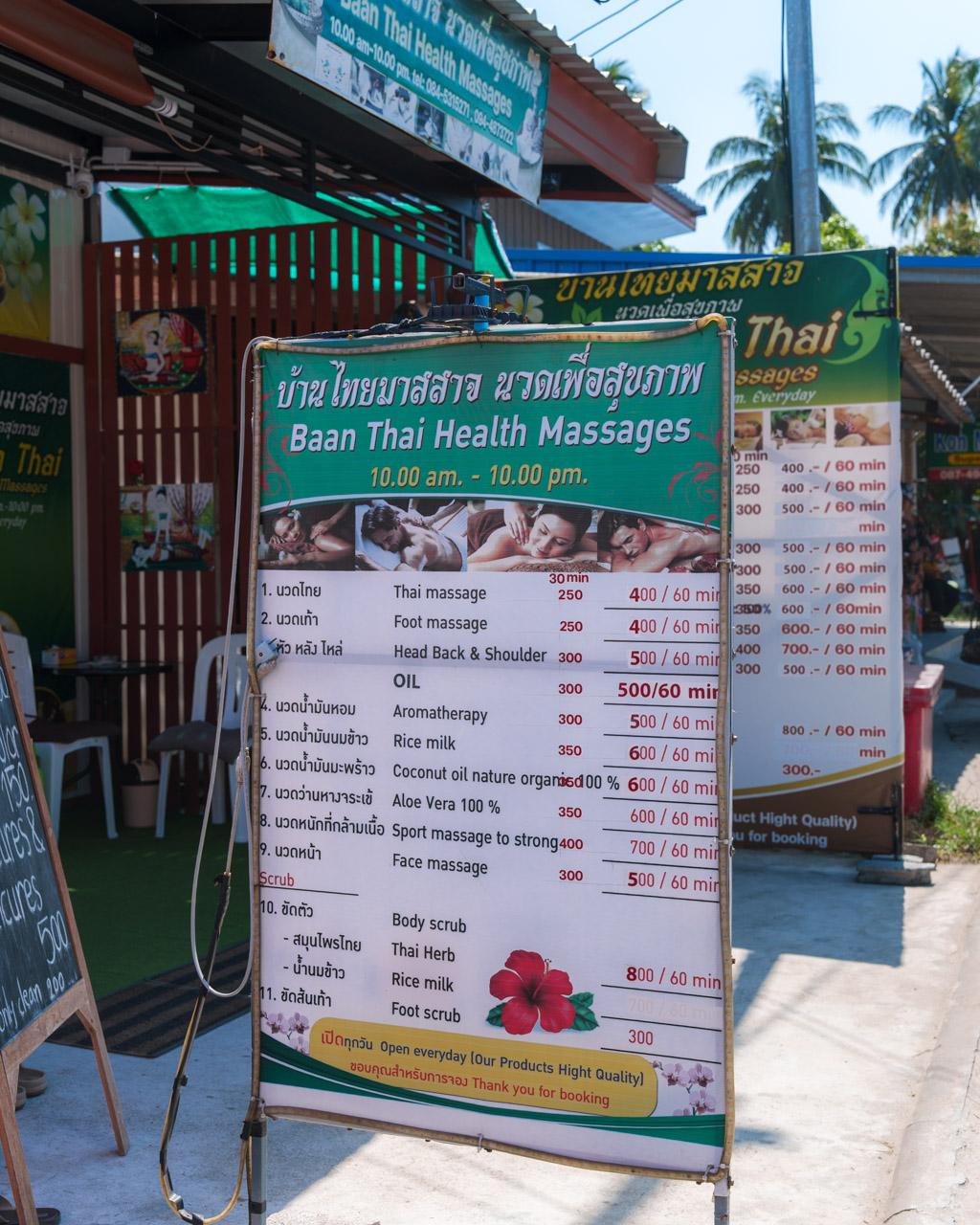 Baan Thai Health Massages storefront sign displaying service menu with prices in Thai baht and hours, Koh Mook, Thailand.