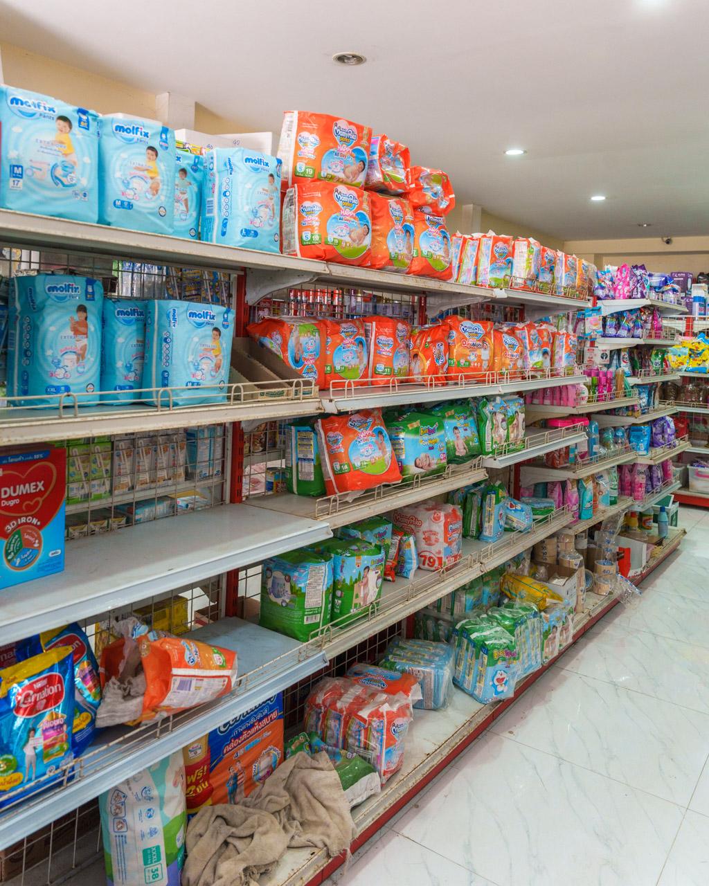 Store shelves displaying blue and orange packaged nappies and baby products in Koh Mook, Thailand.