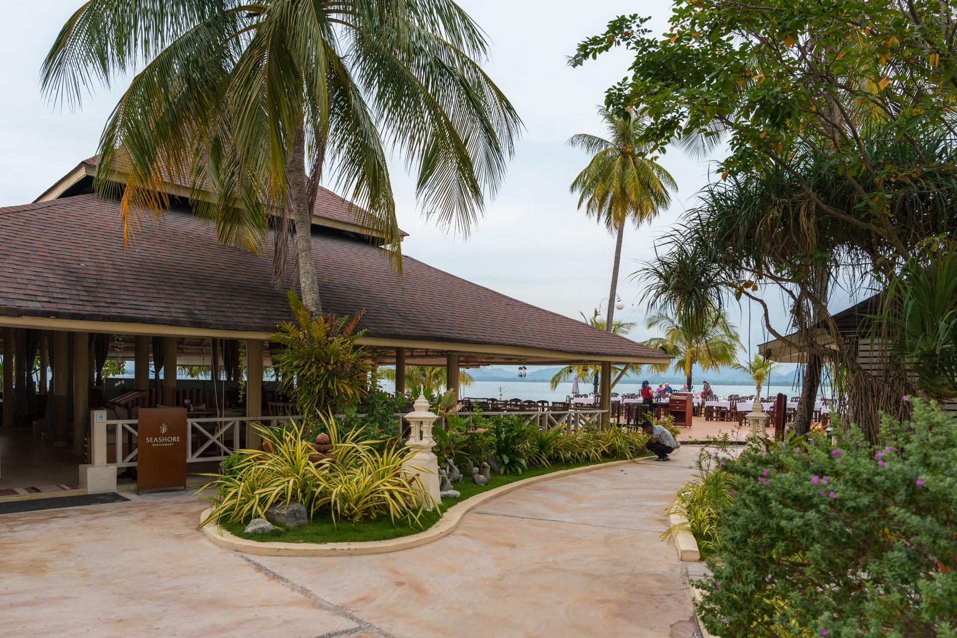 Tropical beachfront restaurant at Sivalai Resort with thatched-roof buildings, palm trees and sea view in Koh Mook, Thailand.