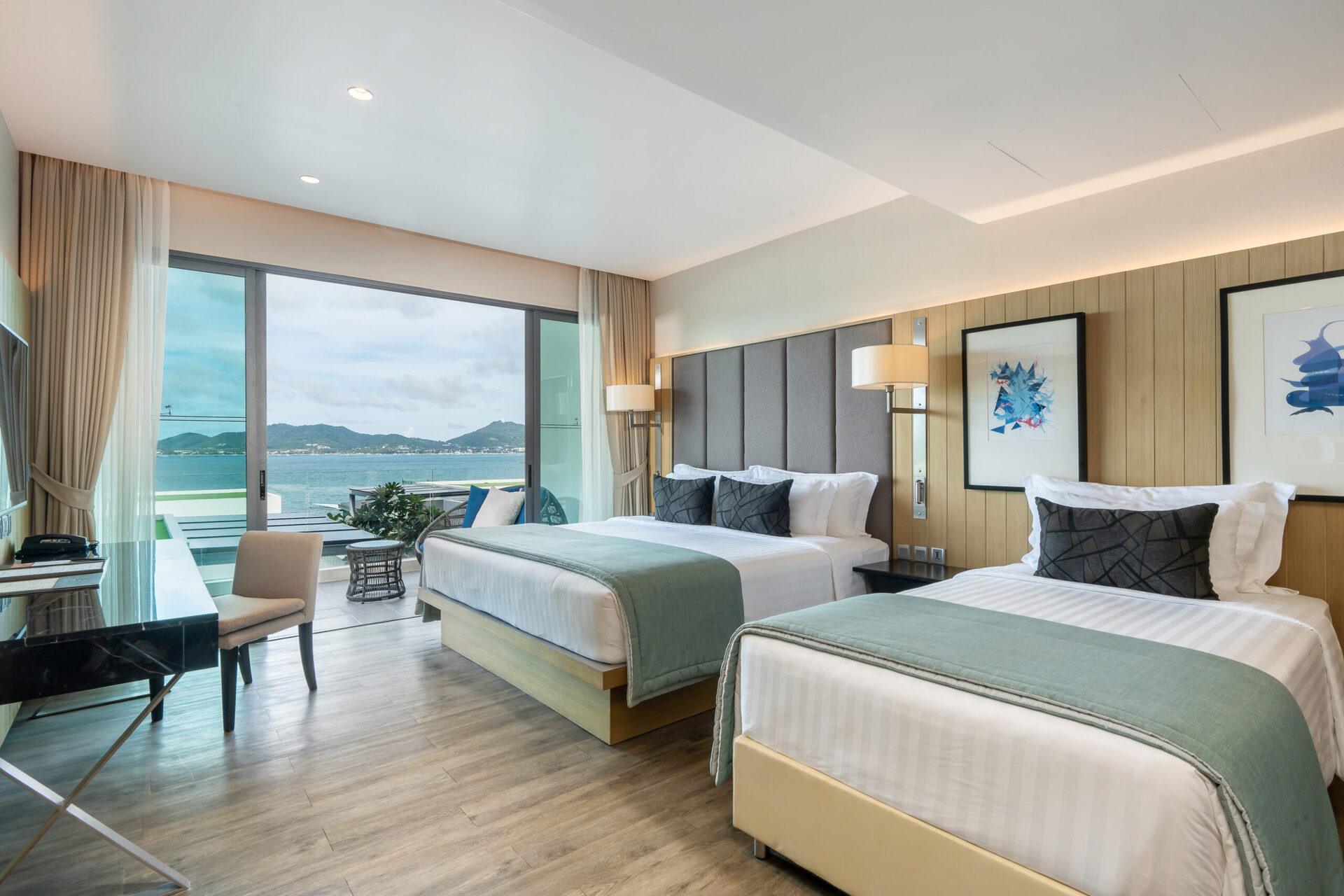 Spacious beachfront family resort room in Phuket with two beds, panoramic sea view balcony, and coastal mountain landscape.