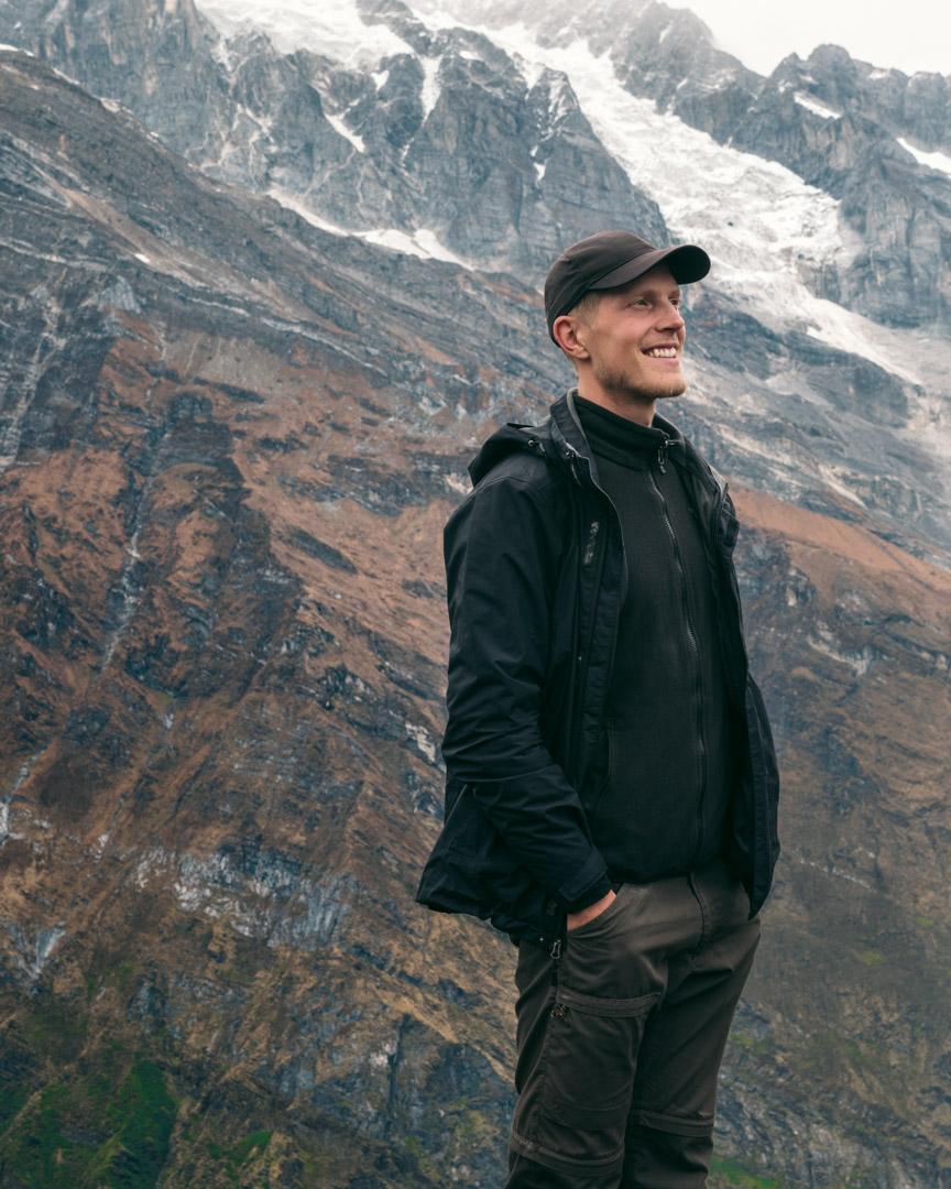 Alex in Nepal in front of huge mountains in the background, looking content