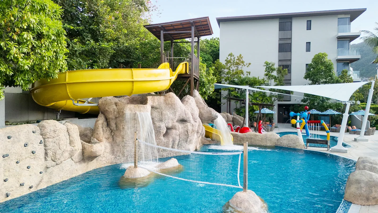 Ozo Phuket resort pool with bright yellow spiral slide, artificial rock formations, waterfall features, and modern white building backdrop.