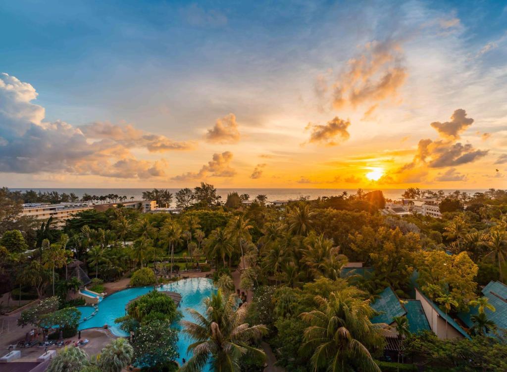 Aerial drone view of Paradox Karon resort at sunset with blue pool, palm trees, and Andaman Sea coastline in Phuket.
