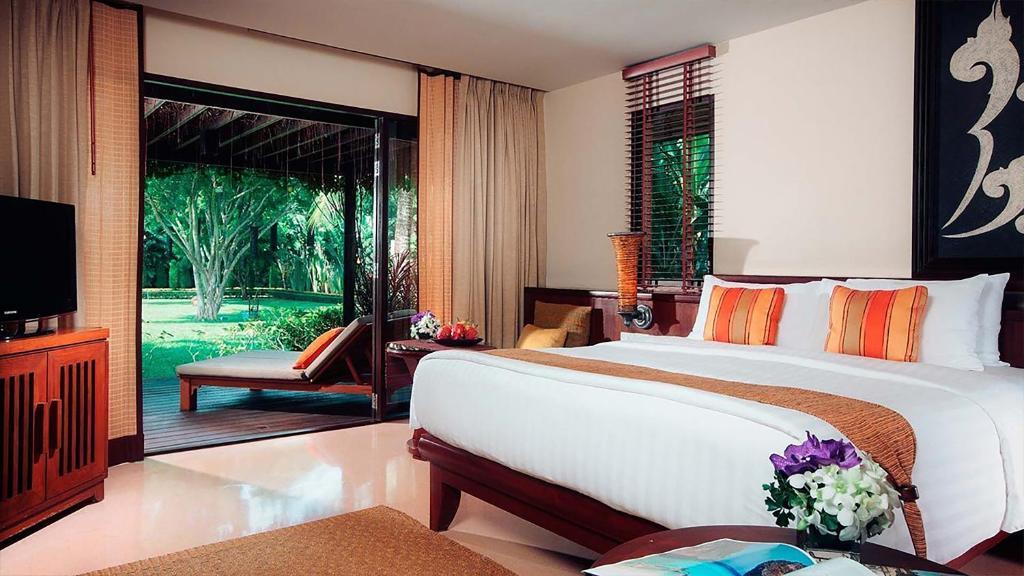 Luxury two-bedroom suite villa bedroom with king bed, orange accents, and garden views through sliding glass doors.