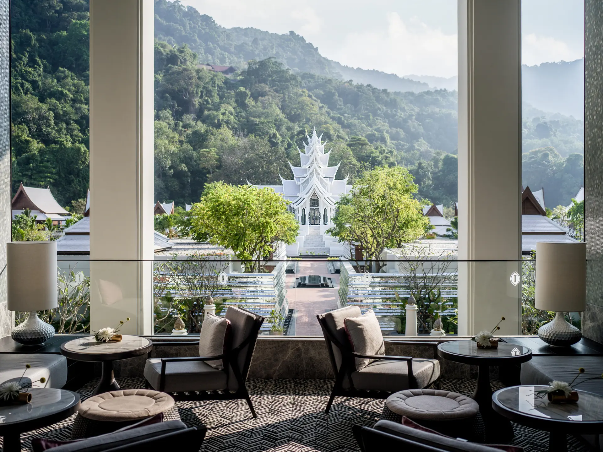 Phuket InterContinental hotel lounge with floor-to-ceiling windows overlooking white temple and forested mountains.