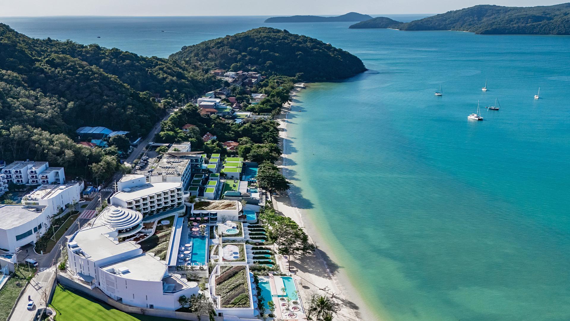 Aerial view of Veranda Resort Phuket on a tropical beach cove with turquoise water, sailboats, and forested hills.