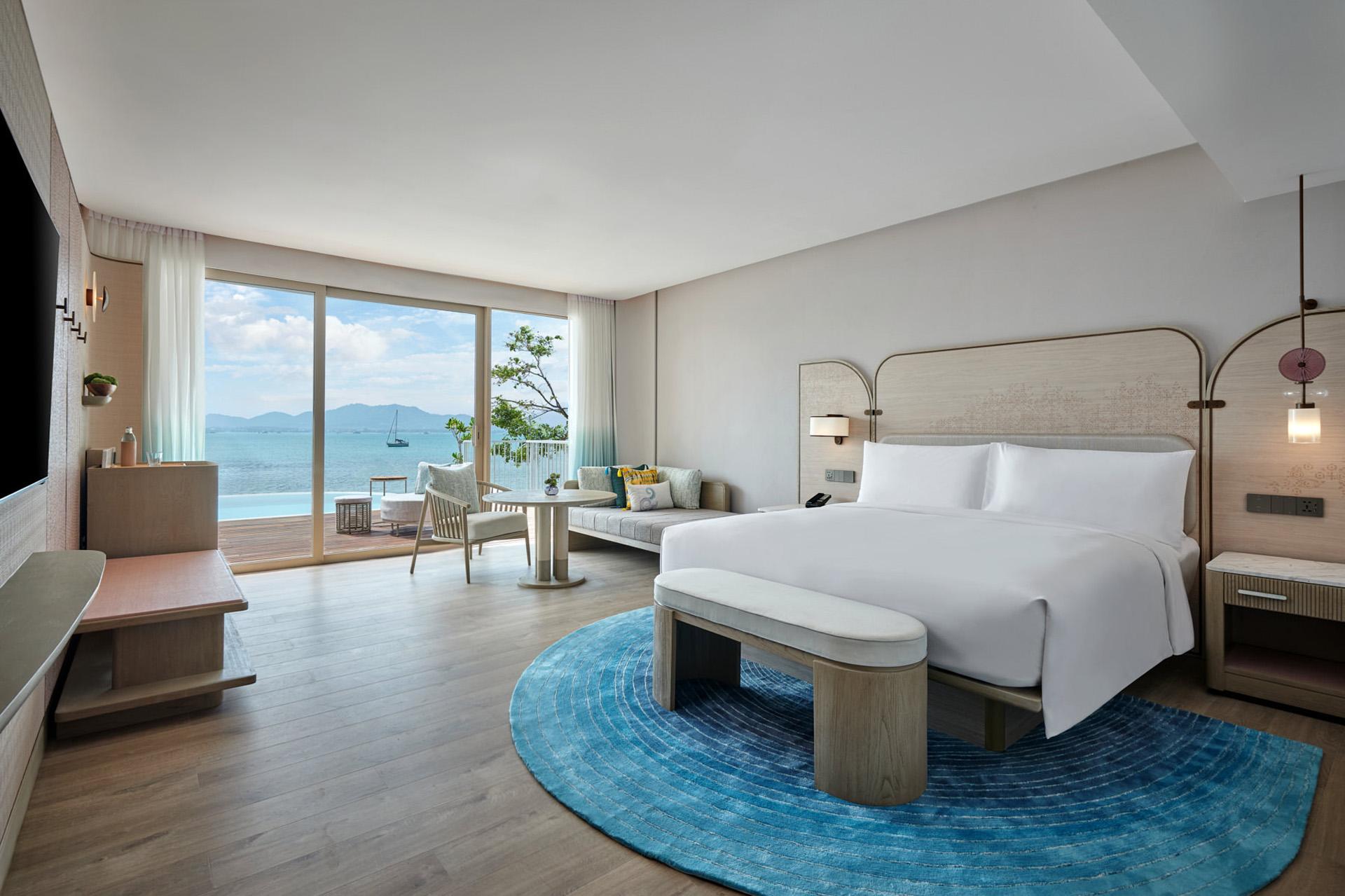 Luxury bedroom with king bed, ocean view balcony overlooking Phuket waters, modern minimalist design, and sitting area.